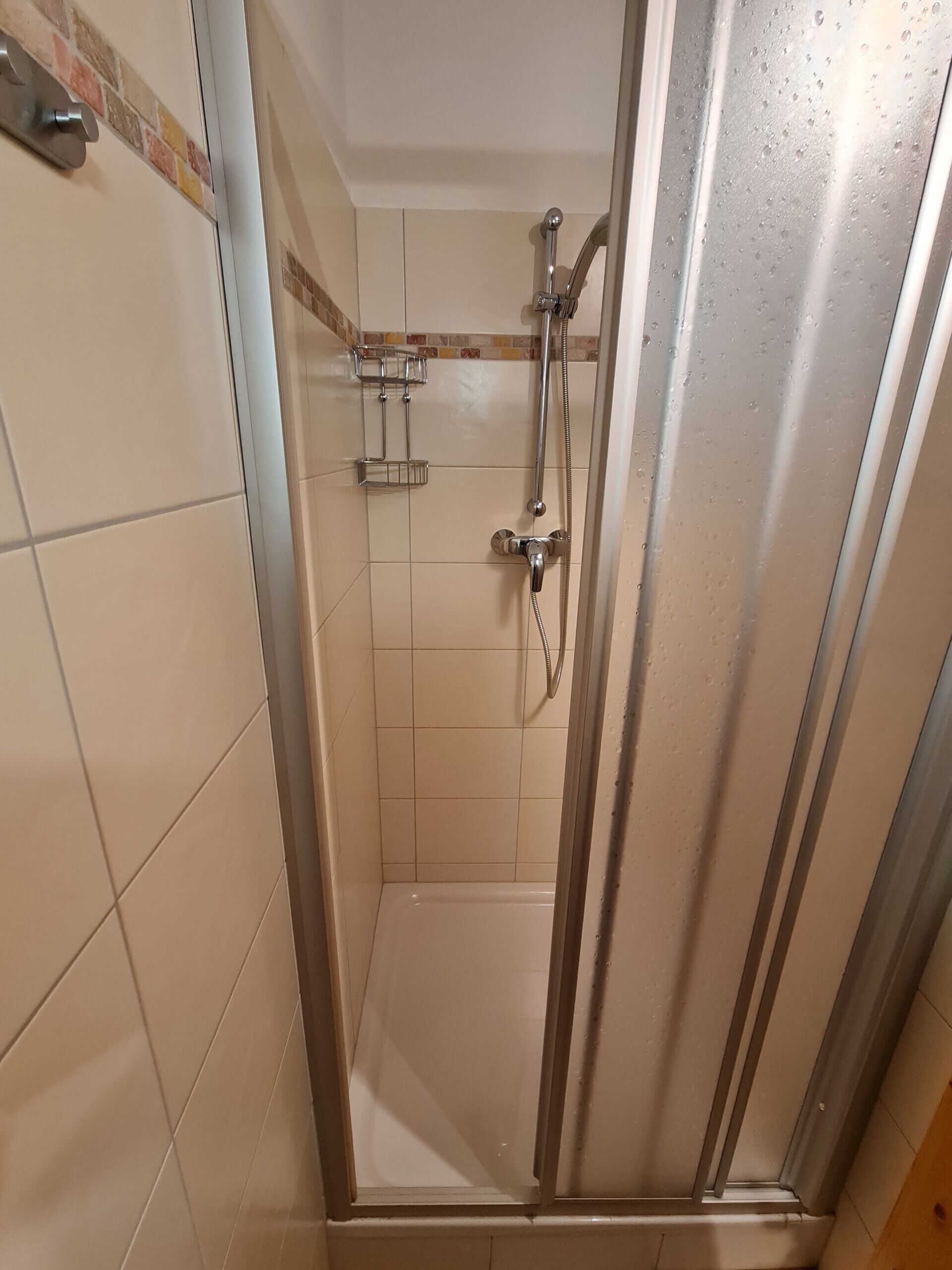A shower with a glass door, a chrome showerhead, and a handheld shower attachment.