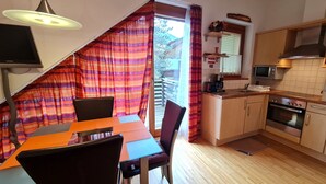 A compact kitchen with a dining area, wooden flooring, and a view through a window with curtains. - Haus Daniela by Globalimmoservice (Bad Kleinkirchheim)