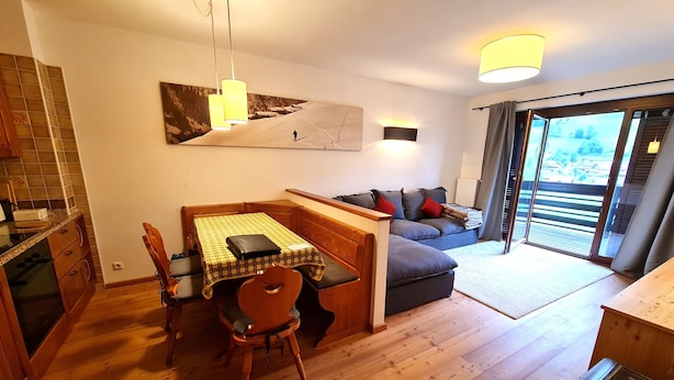 A modern kitchen with wooden cabinets, a dining table with chairs, and a large window overlooking a scenic view.