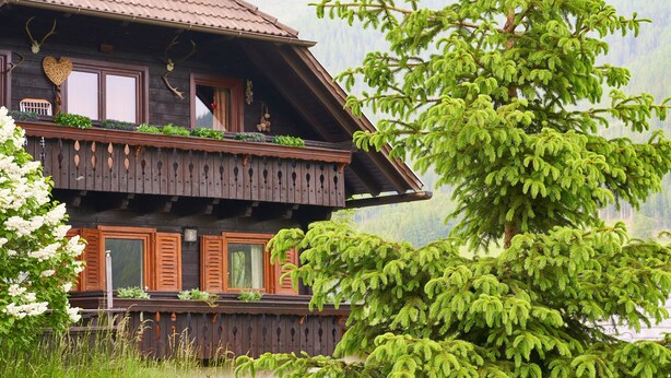 Una casa de madera con balcón, rodeada de vegetación y con vista a la montaña.