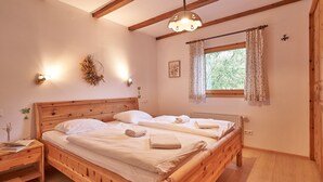 Una cama de madera con ropa de cama blanca, una mesita de noche, una lámpara de pared y una ventana con cortinas.
