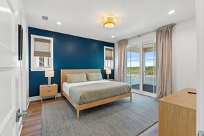Une chambre à coucher comprenant un lit, des tables de chevet, une commode, une coiffeuse et une vue sur l’extérieur.