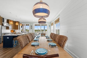A modern kitchen with a central island, pendant lighting, and a dining area with a long table set for six. - The Sea Suite: Lovely Sugar Sands Home- Priv. Pool, Sleeps 18, Game & Movie Room (Mexico Beach)