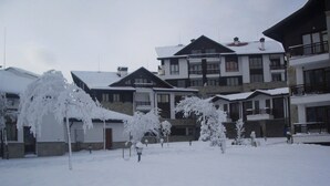 A snow-covered courtyard with multi-story buildings, including balconies and a ski lift visible in the background.