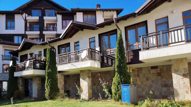 A multi-story residential building with balconies, stone facade, and a well-maintained lawn.