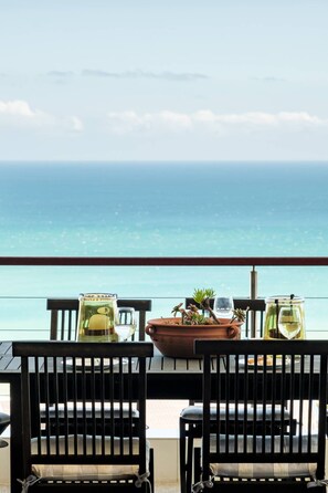 Een balkon met twee houten stoelen, een tafel met een bloempot, een glas en een fles.
