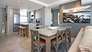 Een moderne keuken met een centraal eiland, een eethoek met stoelen en een groot schilderij aan de muur.