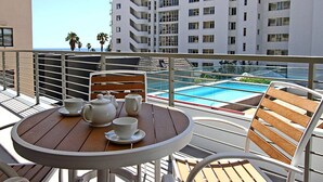 Een balkon met een gedekte tafel voor thee, met uitzicht op een zwembad en een meerlaags gebouw.