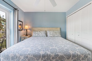 Une chambre à coucher comprenant un lit, une table de chevet, une lampe, un ventilateur de plafond et une vue sur l’extérieur.