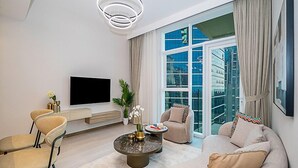 A modern living room with a flat-screen TV, a round coffee table, a sofa, and a chair. - Cozy Luxury 1BR Apt in Business Bay (Dubai)