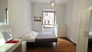 A bedroom with a bed, a bedside table with a lamp, a wardrobe, and a window with a view of buildings. - Latini's Home (Rome)