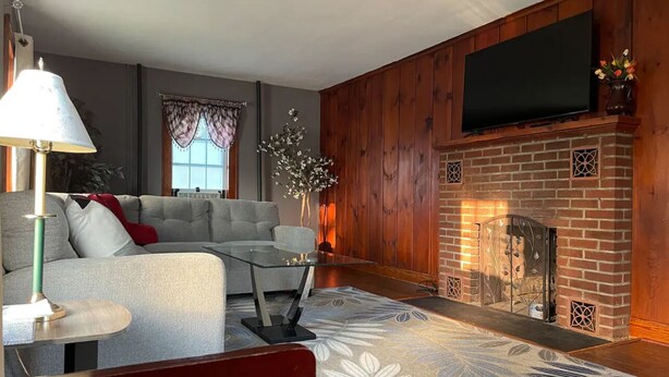 A living room with a sofa, a glass coffee table, a fireplace, and a TV mounted on the wall.