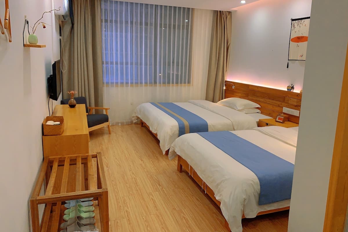 Habitación de hotel con dos camas, un escritorio, una silla, un zapatero de madera y una ventana con cortinas.