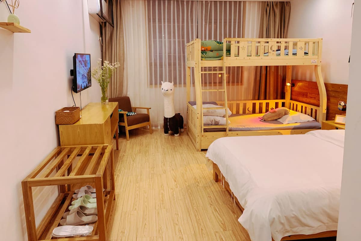 Una habitación de hotel con literas, un escritorio con silla, un televisor y un zapatero.
