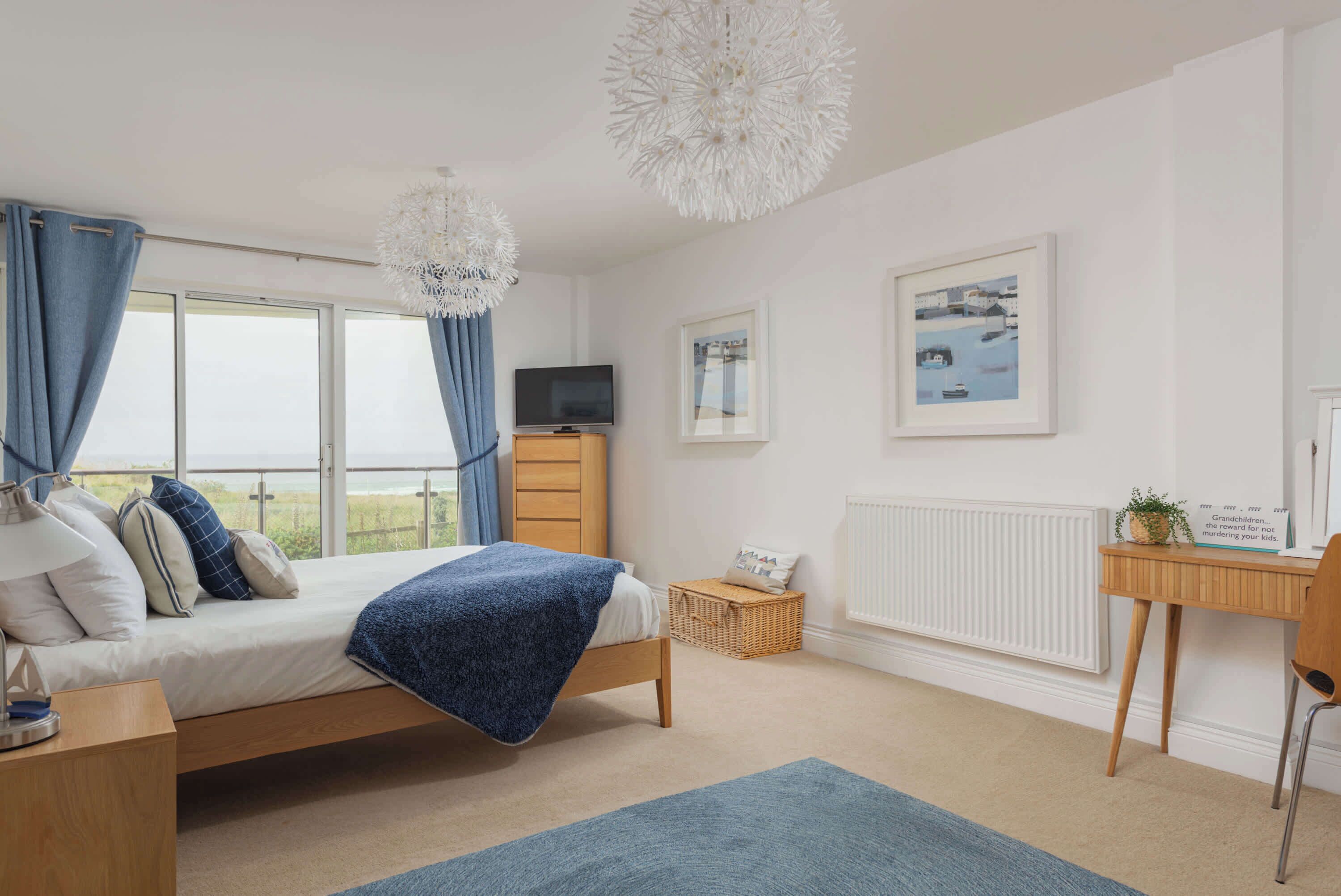 A bedroom with a bed, a television, a desk, and a window with curtains.