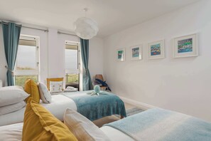 A bedroom with two beds, a window with curtains, a chair, and framed pictures on the wall. - Host & Stay | Sunset (Newquay)