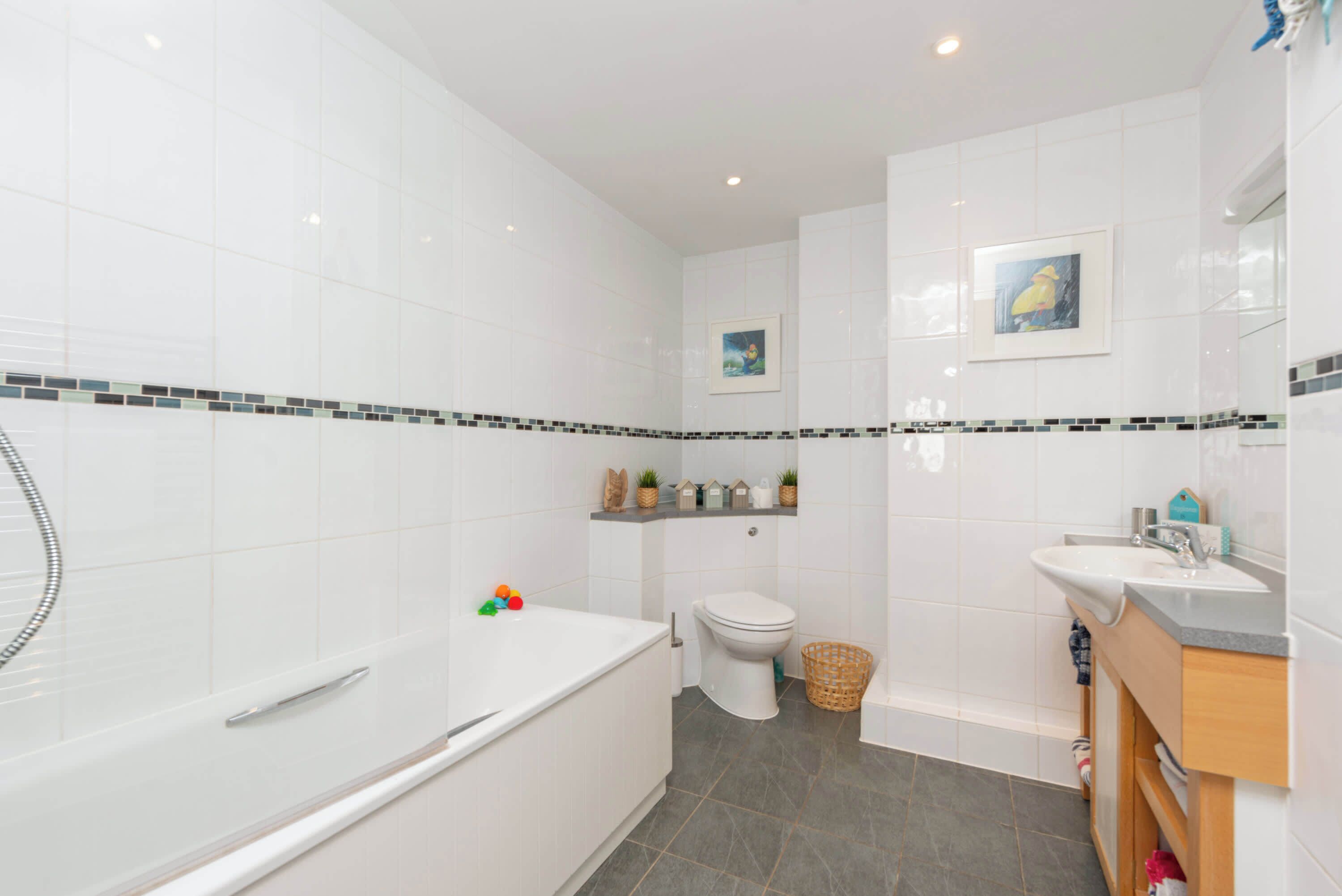 Un baño moderno con azulejos blancos, una bañera, un inodoro y un lavabo.