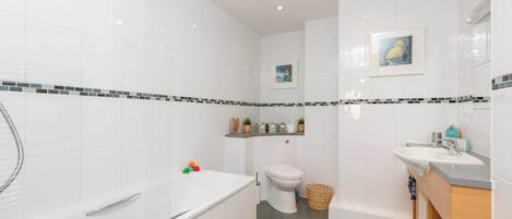 Un baño moderno con azulejos blancos, una bañera, un inodoro y un lavabo.