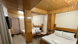 A hotel room with two beds, a small table, and a television. - Hotel Hans (Shimla)