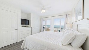 Un dormitorio con cama, televisión, ventilador de techo y vista al océano.
