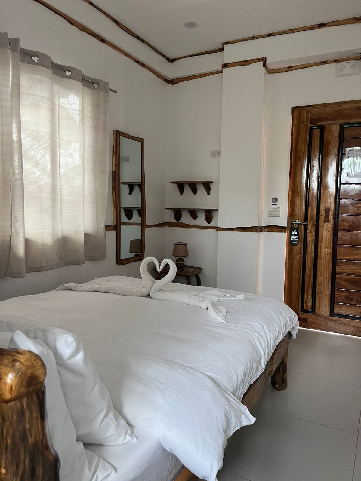 A neatly made bed with white linens and two swan-shaped pillows. There is a wooden door to the right and a mirror on the wall.