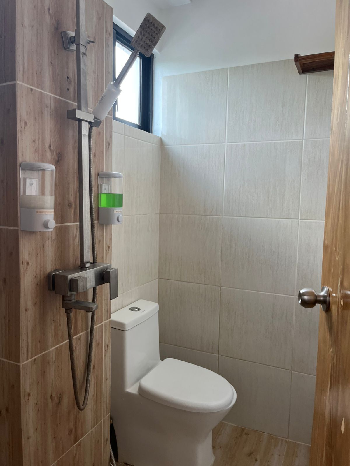 A small, compact bathroom with a shower, toilet, and a window.