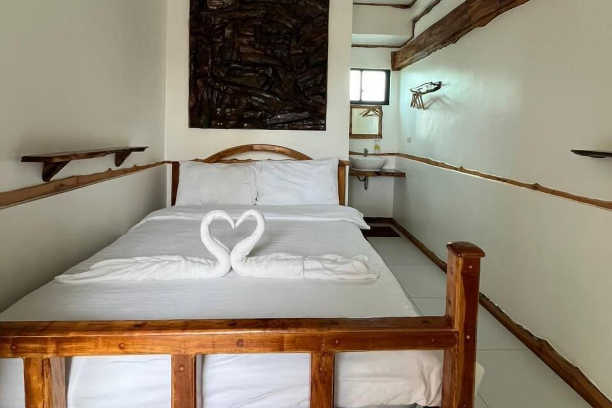 A hotel room with a wooden bed, a large abstract painting on the wall, and a small bedside table with a mirror.