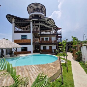 A modern multi-story building with a pool, surrounded by greenery and a clear sky. - The Hat Trick Hostel (Moalboal)