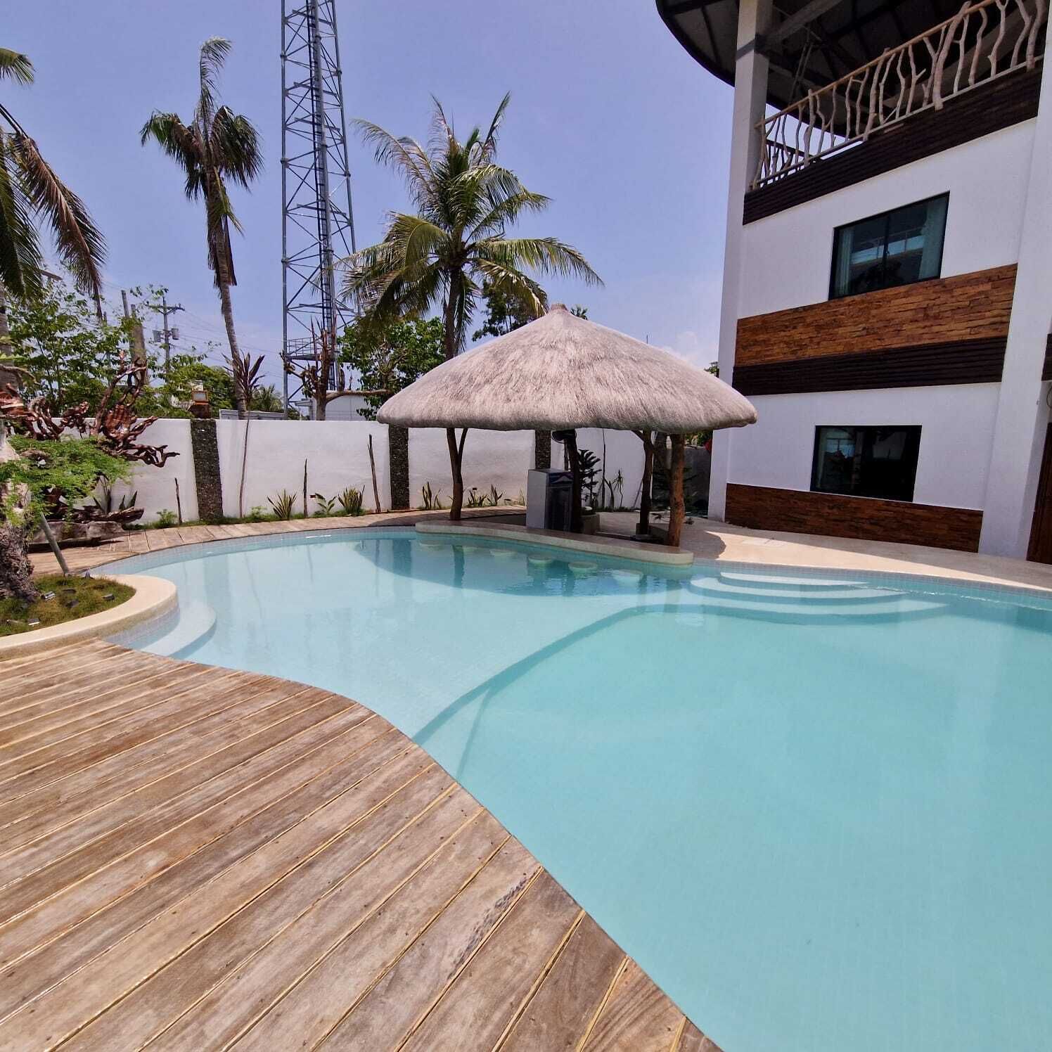A swimming pool with a wooden deck, a thatched umbrella, and a modern building with balconies.