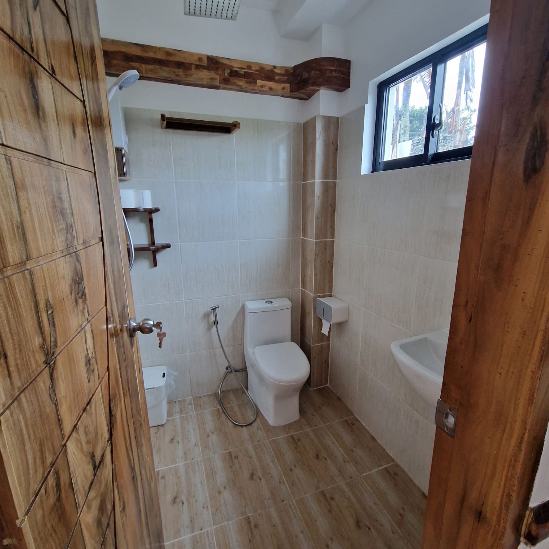 A bathroom with a wooden door, a toilet, a sink, and a window.