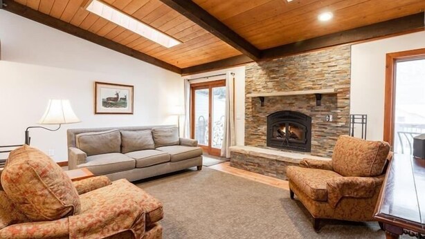A cozy living room with a stone fireplace, wooden ceiling beams, and a sofa. - 3-Bedroom Meadow Creek Townhom 3 Townhouse (Vail)