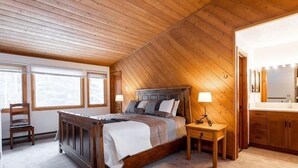 A bedroom with a wooden ceiling, a bed with a wooden headboard, bedside tables, a chair, and a large window. - 3-Bedroom Meadow Creek Townhom 3 Townhouse (Vail)