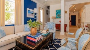 Un salón con un sofá, una mesa de centro con libros, una planta y una alfombra azul estampada.