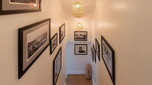 Un pasillo con fotografías enmarcadas en las paredes, una escalera de madera y un colgador con luz.