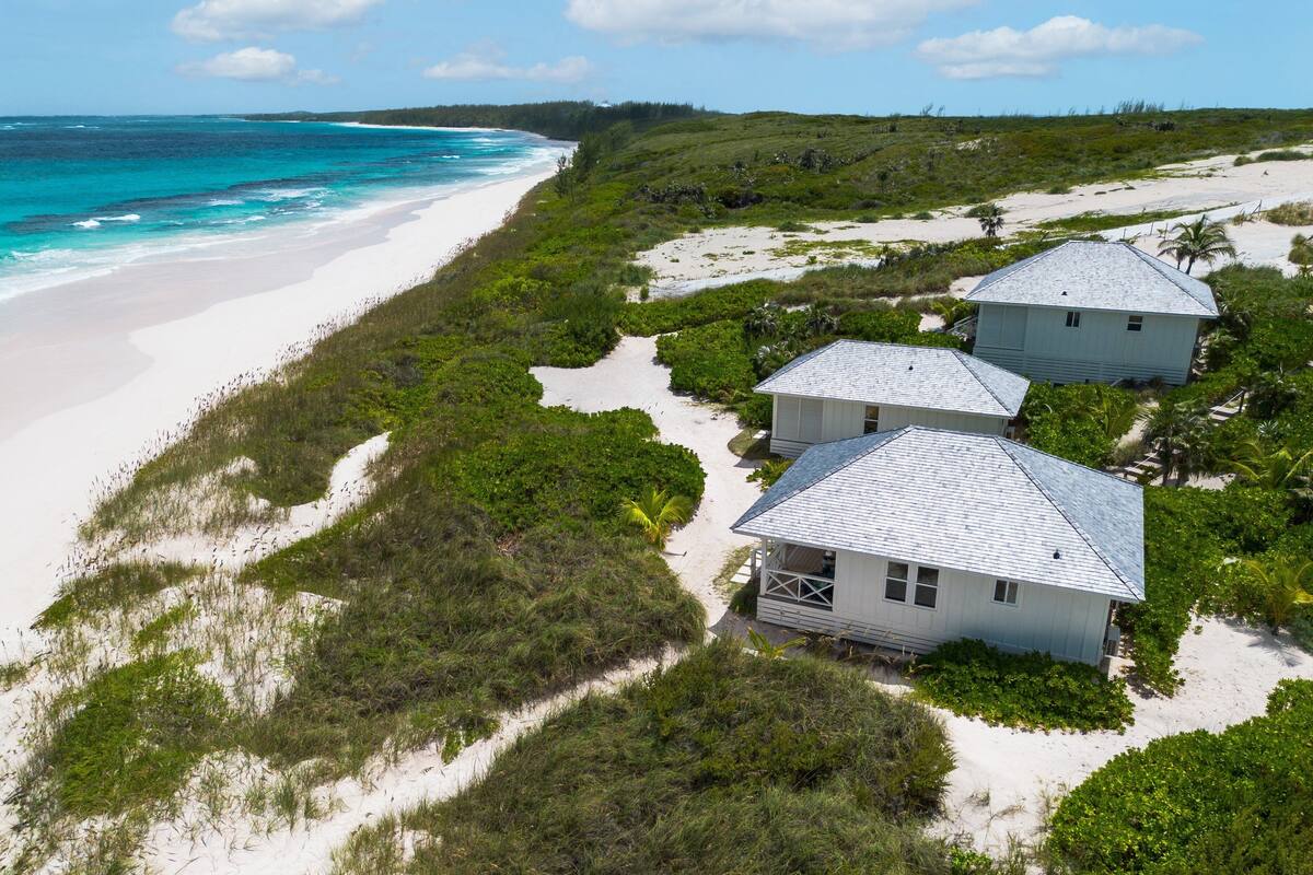 A beachfront property with two white buildings, a sandy beach, and ocean views.
