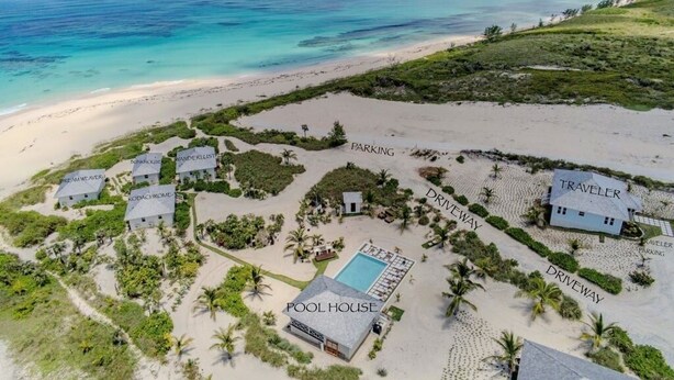 Vista aerea di una proprietà fronte spiaggia con una dependance con piscina, diverse case per gli ospiti e vialetti che conducono alle aree di parcheggio.