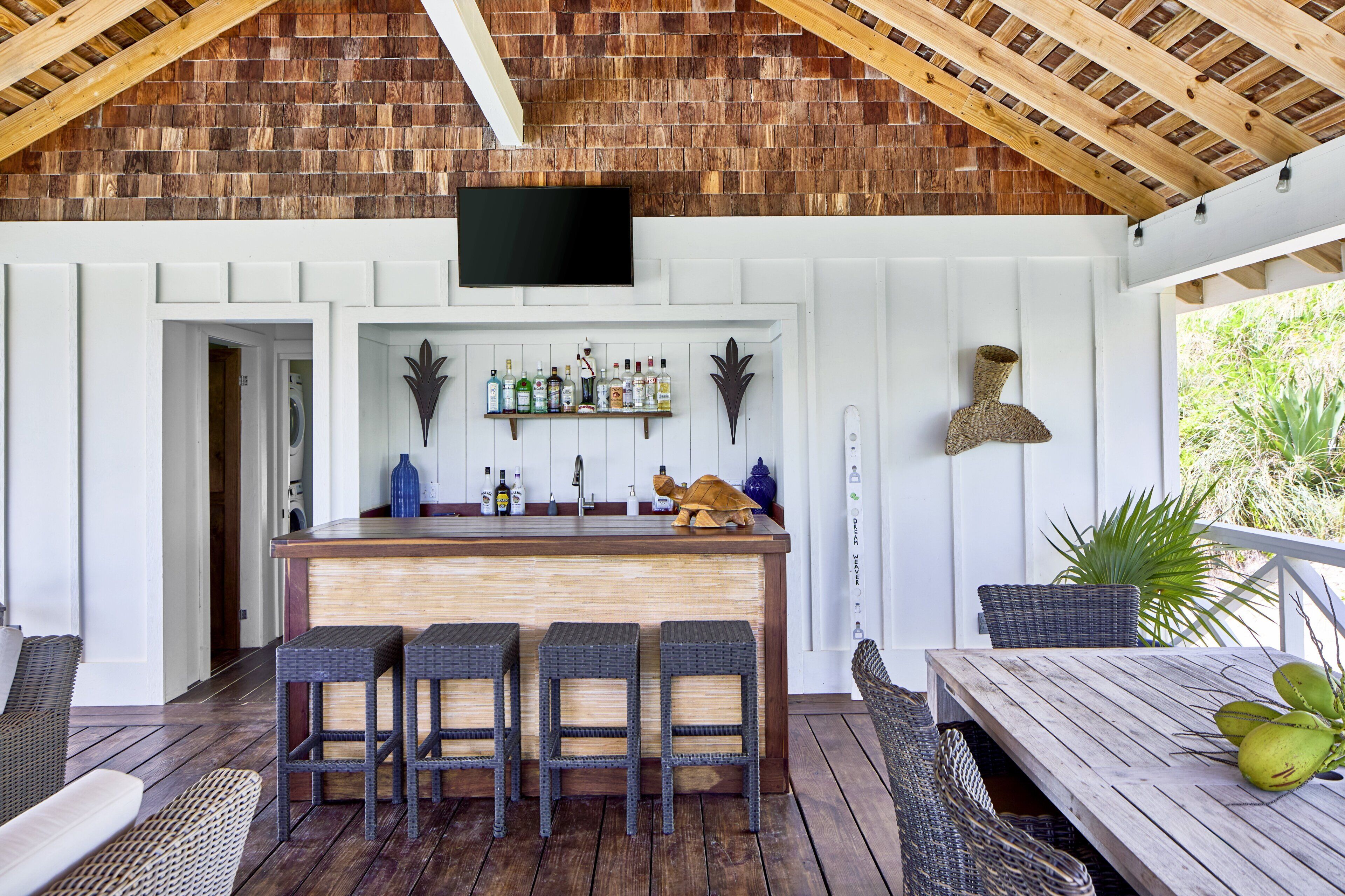 A covered outdoor bar area with a wooden ceiling, a flat-screen TV, a bar counter, and seating.