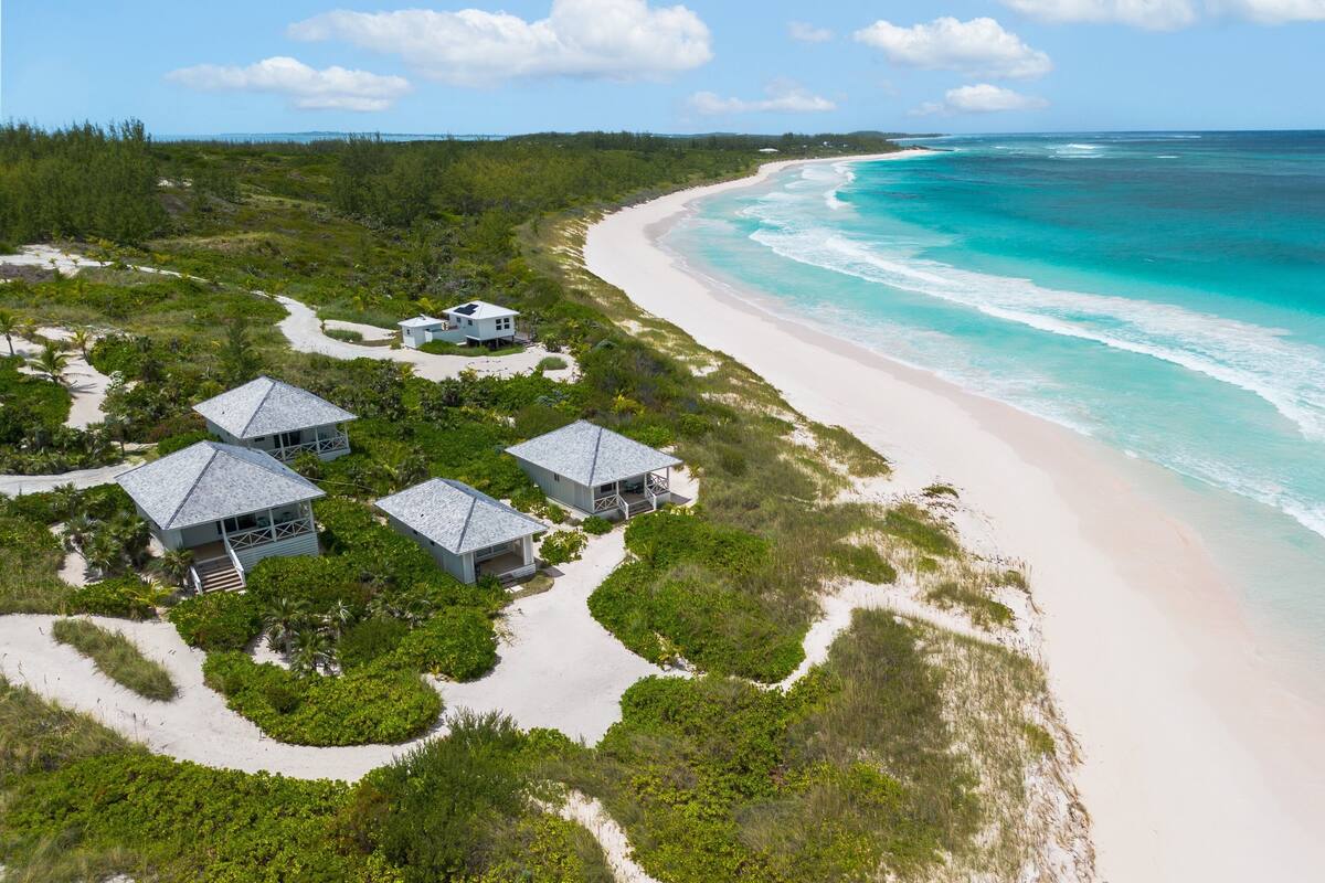 An aerial view of a beachfront property with several buildings, a sandy beach, and a clear view of the ocean.