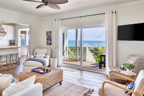 A spacious living area with a large sliding glass door leading to a balcony with a view of the ocean. - Bohemia Bungalows (Governor's Harbour)