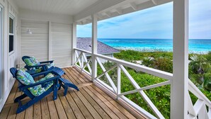 Un portico coperto con due poltrone Adirondack blu, un pontile in legno e vista sull'oceano.