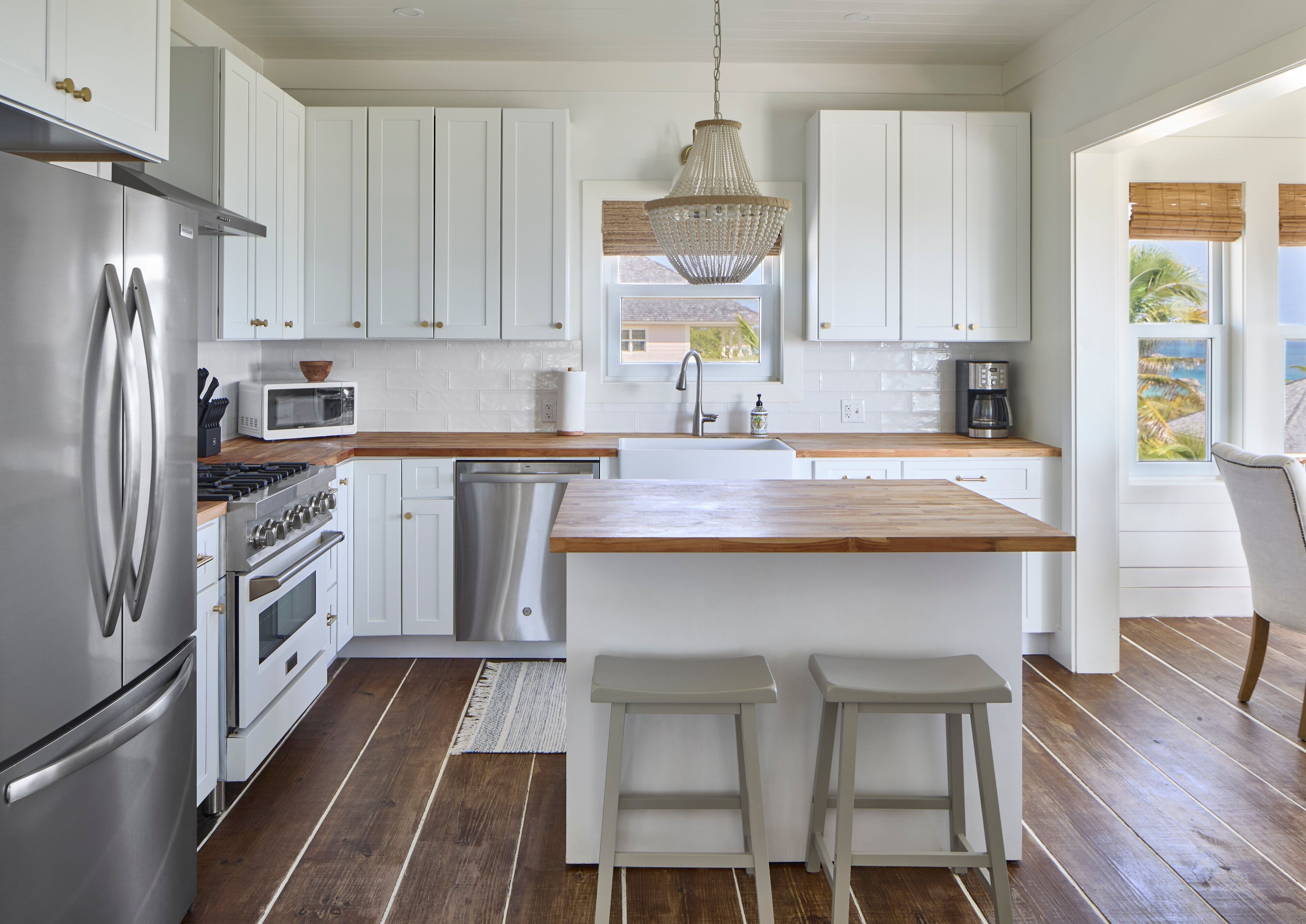 Une cuisine moderne avec des meubles blancs, des appareils en acier inoxydable, un plan de travail en bois et un grand îlot central doté de tabourets.