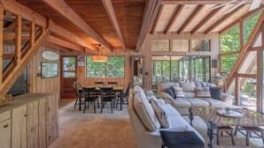 A spacious wooden cabin interior with a dining area, a large sofa, and a ceiling fan.