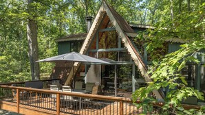 A cabin with a deck, outdoor seating, and a large umbrella.