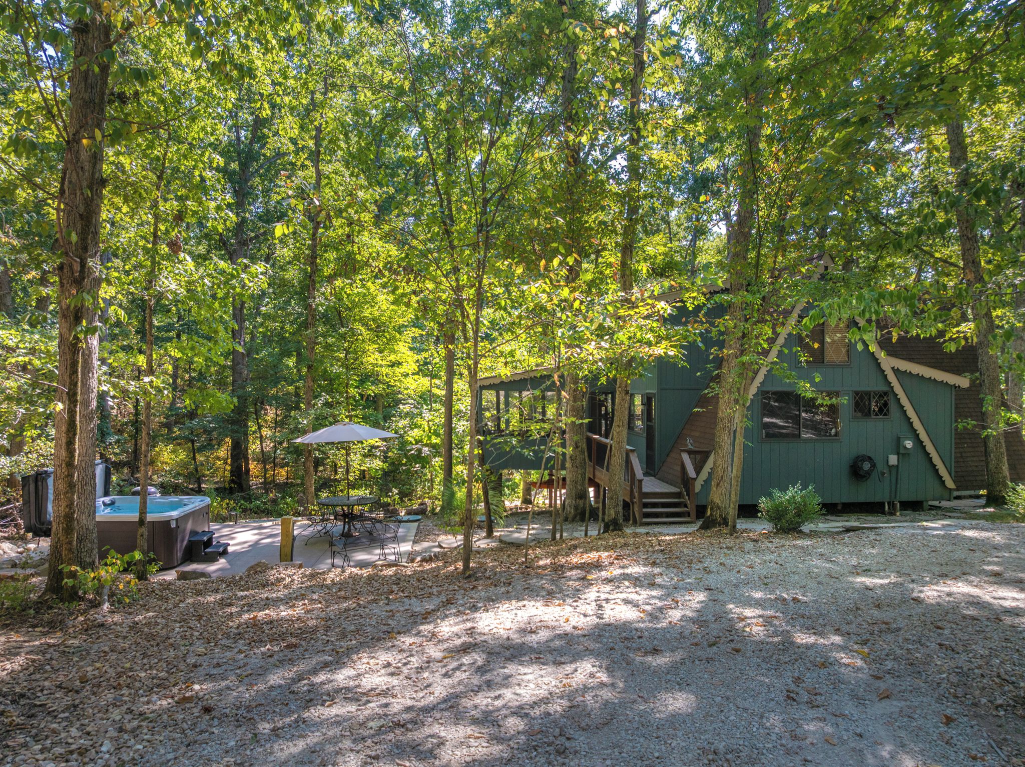A rustic cabin with a covered outdoor seating area, a hot tub, and a staircase leading to a deck.