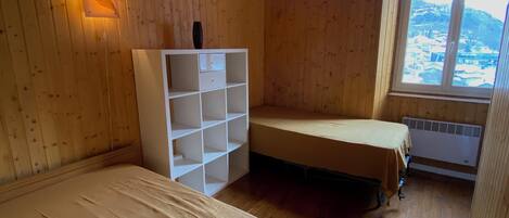 A wooden room with a bunk bed, a white shelving unit, and a window overlooking a snowy landscape.