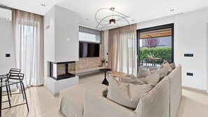 A modern living room with a sofa, a TV, a fireplace, and a view of the outdoors. - Charming Villa Vallis with swimming pool, jacuzzi and sauna (Kadumi)