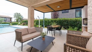A covered outdoor patio with a pool, a sofa, a table, and chairs. - Charming Villa Vallis with swimming pool, jacuzzi and sauna (Kadumi)