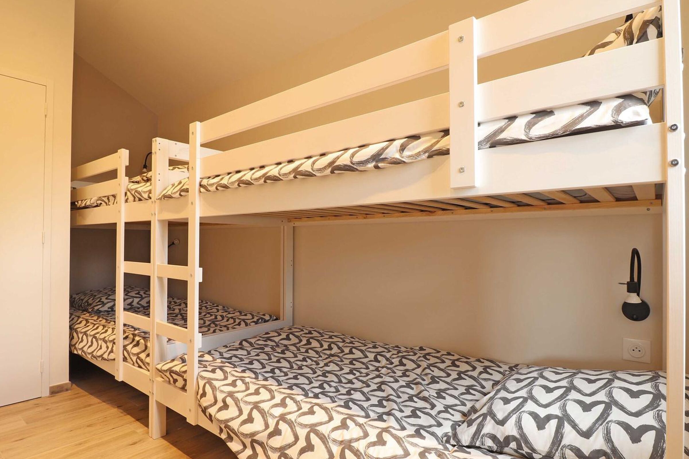 A bunk bed room with patterned bedding and a wall-mounted lamp.