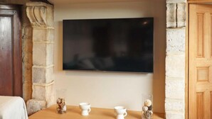 Una habitación con un televisor fijado en una pared de piedra, una mesa de madera con dos tazas blancas, y un mueble de madera a la izquierda.