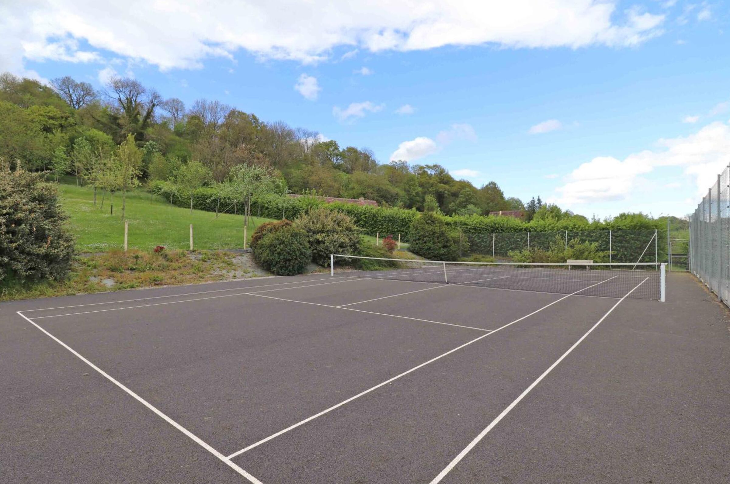 Ein Tennisplatz im Freien mit Netz, umgeben von Grünflächen und Bäumen.